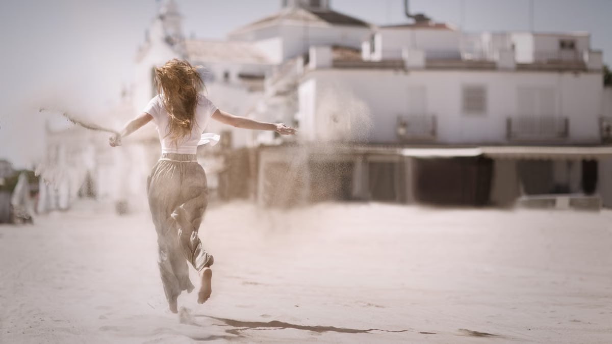 Back view of a young woman jumping and enjoying on a sunny beach, embodying freedom and happiness.